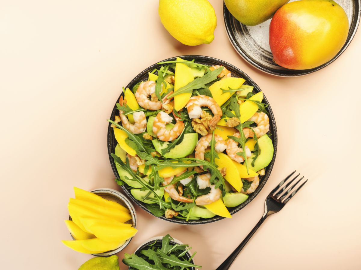 Seafood salad with mango shrimps avocado walnut spinach arugula top view pink background